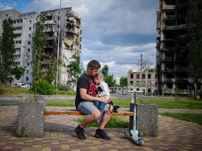 Un hombre con una niña en brazos, sentado frente a edificios destruidos en Borodianka, el pasado 15 de junio.