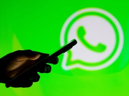 Un usuario maneja un móvil frente al logo de WhatsApp.