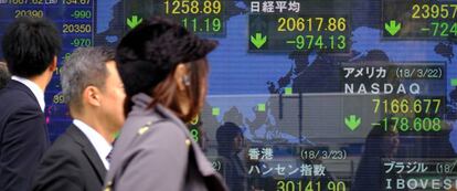 Varios peatones pasan delante de un panel con cotizaciones bursátiles en Tokio (Japón).