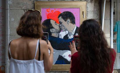 Dos mujeres fotografían la obra del artista urbano Salvatore Benintende, donde Pedro Sánchez y Pablo Iglesias se dan un beso, en Barcelona.