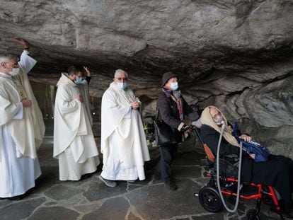 Un grupo de sacerdotes acompaña a una enferma en silla de ruedas en la entrada de la gruta del Santuario de Lourdes, en Francia, donde cada año acuden miles de peregrinos en busca de una curación para sus enfermedades.
