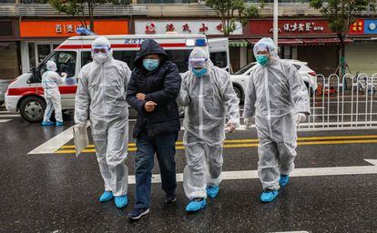 Tres médicos, de blanco, acompañan a un paciente enfermo al hospital de Wuhan, en China.