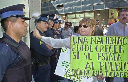 Una manifestante contra el &#039;corralito&#039; golpea un cuchar&oacute;n contra la fachada de un banco protegido por pol&iacute;c&iacute;as en 5 de abril de 2002 en Buenos Aires.