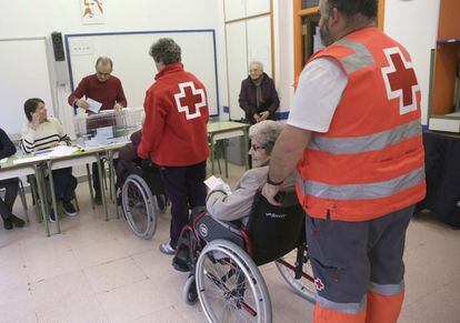 Dos trabajadores de la Cruz Roja acompañan a dos ancianos para que puedan ejercer su derecho a voto en un colegio electoral de San Sebastián.