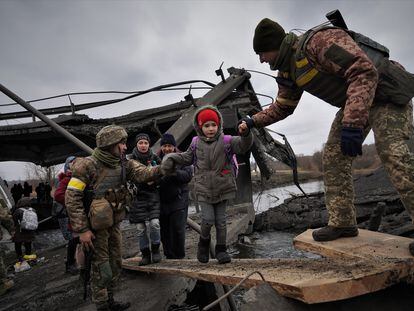 Unos soldados ayudan a una menor a cruzar el puente de Irpín, cerca de Kiev, en marzo.