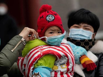 Una mujer pone una mascarilla a un bebé en Pekín, este domingo. En vídeo, más de 300 muertos en China, mientras disminuye el índice de gravedad.