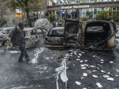 Un hombre camina junto a una hilera de coches carbonizados tras
 los disturbios del jueves, en un suburbio de Estocolmo. 