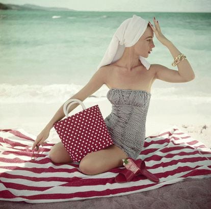 Model seated on striped beach towel wearing grey and white patterned strapless bathing suit. (Photo by Roger Prigent/Condé Nast via Getty Images)