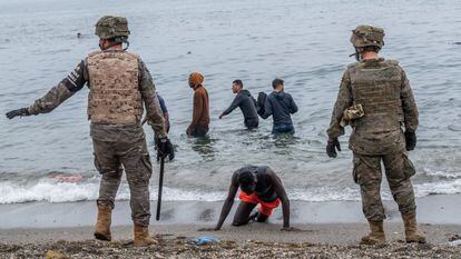 Un hombre arrodillado en una playa de Ceuta mientras el Ejército acordona la zona, el pasado martes.