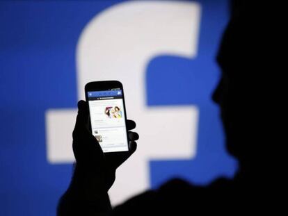 Una persona consulta su tel&eacute;fono m&oacute;vil delante de un logotipo de Facebook.
 