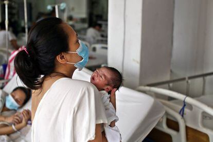 Una mujer intenta calmar a su bebé recién nacido en una sala posparto del hospital Jose Fabella, en Manila, donde en dos camas unidas suelen descansar hasta cinco madres con sus pequeños.