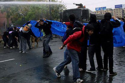 Estudiantes se protegen de un carro lanza aguas de la policía hoy durante una protesta en Santiago de Chile.