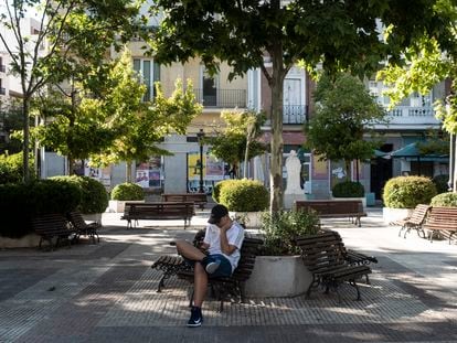 Un joven consulta su teléfono móvil en una plaza vacía del distrito de Chamberí (Madrid).