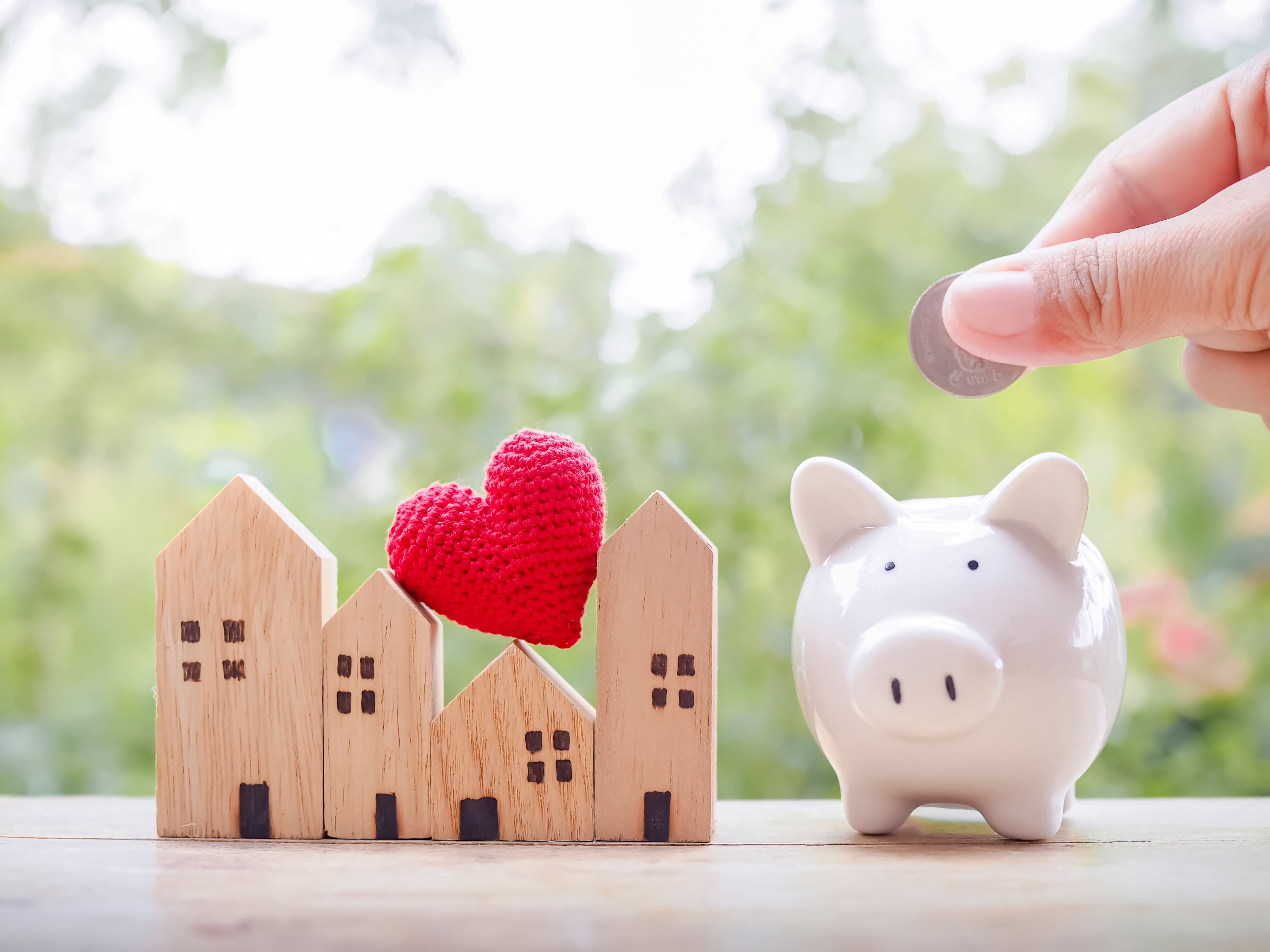 Cierre la mano poniendo monedas en una alcancía y una casa en miniatura, el concepto de ahorro para la casa y la propiedad.
