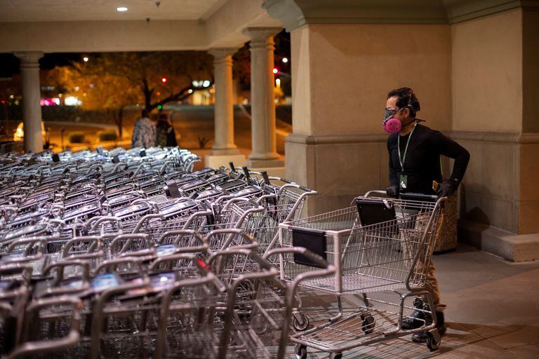 Un hombre con mascarilla apila carritos de supermercado.