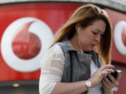Una usuaria maneja su m&oacute;vil junto a una tienda de Vodafone.