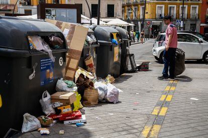 Un hombre mira los contenedores de reciclaje llenos de la plaza de Tirso De Molina, en Madrid.