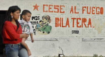 Una mujer pasa junto a su hijo ante un cartel sobre el proceso de paz en el departamento de Cauca, Colombia.