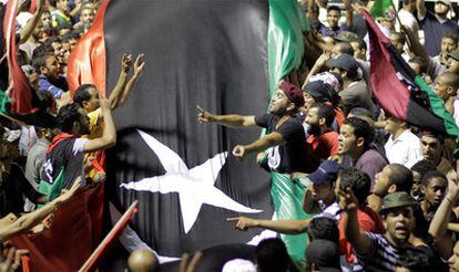 Decenas de libios sostienen una bandera para celebrar la toma de la fortaleza de Gadafi, Bab al-Aziziya, en Trípoli.