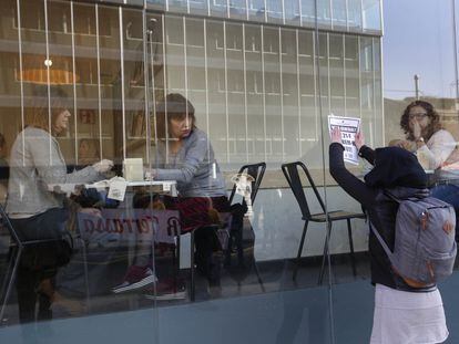 Unas mujeres miran a una chica colocar un cartel en una cafetería de Terrassa.