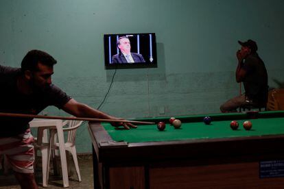 Un hombre mira atentamente la entrevista de Bolsonaro del lunes pasado mientras otro juega billar, a las afueras de Brasilia.