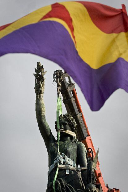 Una grúa retira la <i>Victoria</i> de Franco mientras banderas republicanas lo celebran.