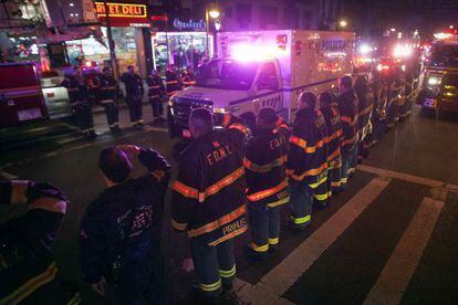 La ambulancia con los agentes asesinados pasa frente una guardia de honor de los bomberos.