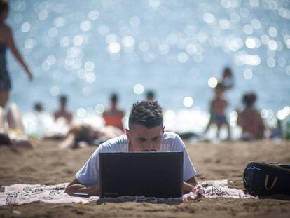 Una persona utiliza su ordenador en la playa de la Barceloneta. 