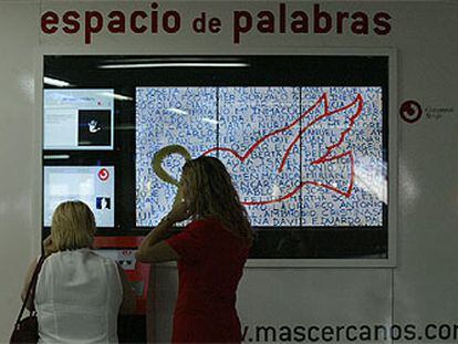 Dos personas, frente a la pantalla del <i>Espacio de palabras,</i> el montaje que sustituirá al <i>santuario</i> de Atocha en homenaje a las víctimas del 11-M.