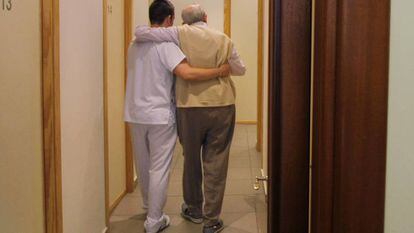 Un auxiliar ayuda a una persona mayor en un centro de d&iacute;a de Sevilla.
