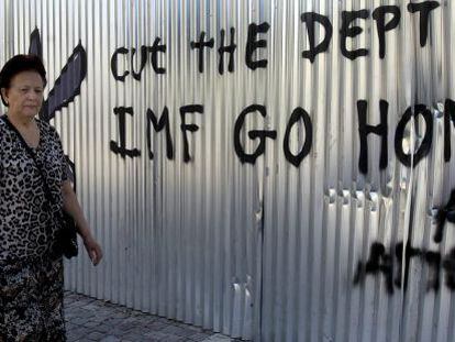 Una mujer camina junto a un grafiti en el que se puede leer &quot;FMI vete a casa, corta la deuda&quot; en Atenas.