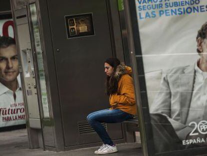 Una joven espera al autob&uacute;s en una marquesina con carteles electorales de Mariano Rajoy (azul) y Pedro S&aacute;nchez (rojo). 