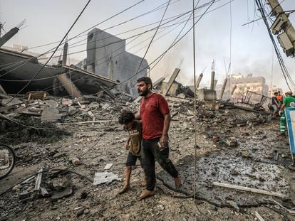 Un hombre camina con su hijo sobre los escombros producidos por un bombardeo israelí sobre Gaza.