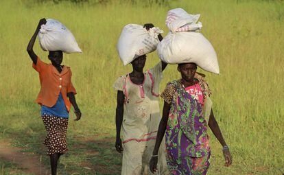 Mujeres sursudanesas regresan a sus casas tras recibir sacos de asistencia alimentaria.