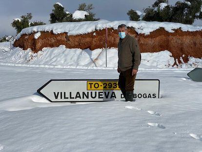 Un vecino de Villanueva de Bogas (Toledo) frente al rótulo de acceso al pueblo, semicubierto de nieve.