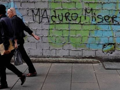 Dos personas caminan este sábado en Caracas por delante de una pintada en la que se lee "Maduro, Miseria".
