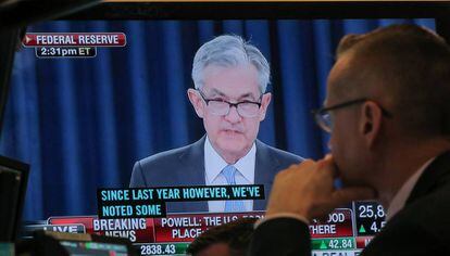 En la pantalla el presidente de la Reserva Federal, Jerome Powell, bajo la mirada de un agente de Bolsa en el parqué de la Bolsa de Nueva York