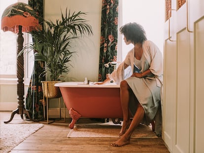 Una mujer se prepara para una baño rodeada de decoración y plantas.