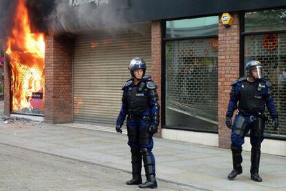 Dos policías vigilan una tienda incendiada durante los disturbios registrados ayer en Manchester.