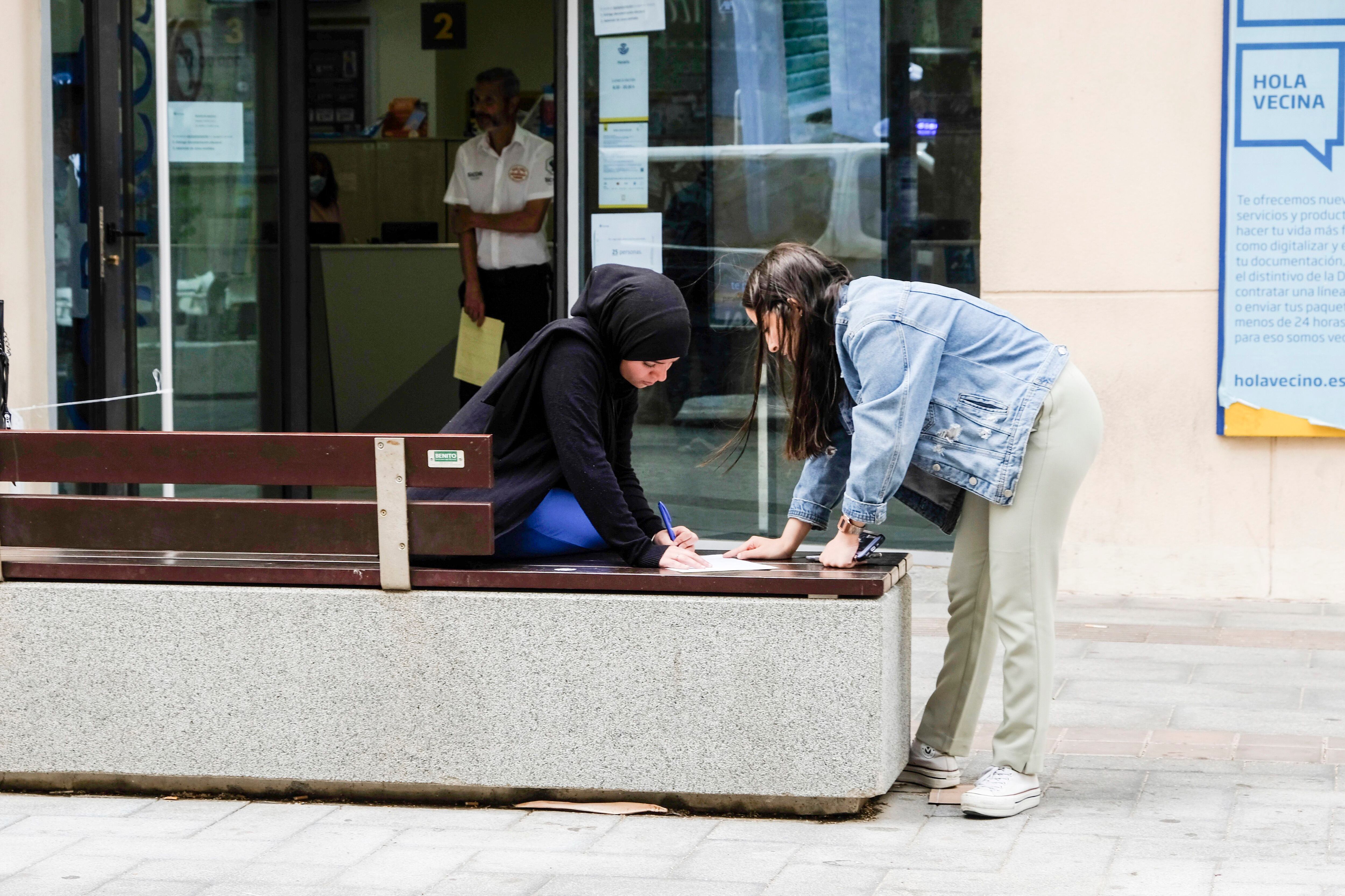 Dos mujeres rellenan el impreso para solicitar el voto postal delante de la Oficina de Correos de Melilla, este jueves. 