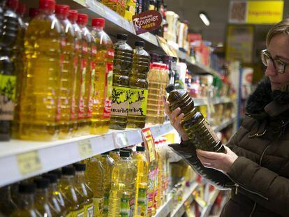 Una mujer mira varias botellas de aceite de oliva en un supermercado.