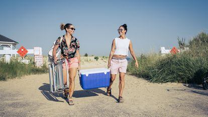 Two women carry a cooler to the beach