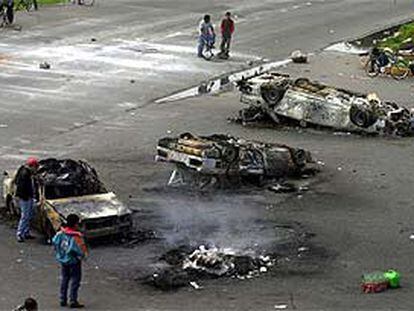 Campesinos de San Salvador Atenco bloquean una carretera junto a varios coches de policía quemados.