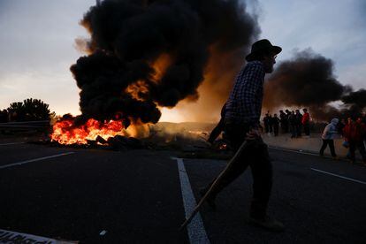A man walks near a fire, as farmers block the AP-7 highway during a protest over price pressures