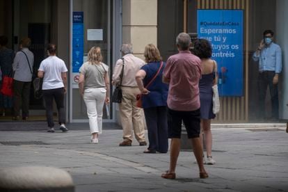 Varias personas esperan su turno en la calle para entrar en un banco en Sevilla, este lunes.