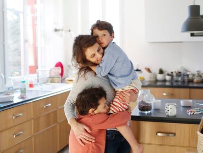 Una madre abraza con fuerza a sus hijos en la cocina.