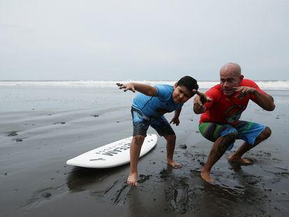 Surfing instructor Ernesto Soriano and Mariano Pineda, a child, prepare to ride waves as they participate in the Surftismo program, an alternative therapy for children with autism spectrum disorder diagnoses that uses surfing, in Chiltiupan, El Salvador August 14, 2022. REUTERS/Jose Cabezas
