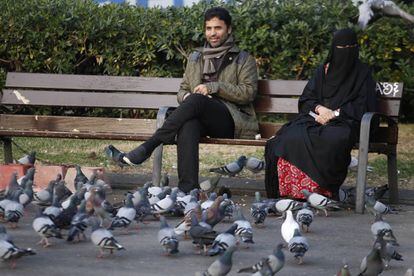 Una mujer ataviada con Burka sentada en el banco de un parque.
