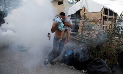 Un hombre escapa con un niño en brazos del gas lacrimógeno lanzado por los antidisturbios el domingo 29 de septiembre en el campo de refugiados de Moria, en la isla griega de Lesbos.