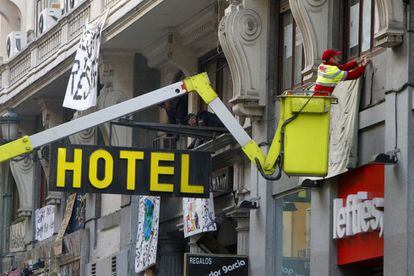 Un trabajador retira los carteles que cuelgan de las ventanas del Hotel Madrid, tras ser desalojado hoy por la Policía junto a las viviendas aledañas al teatro Albeniz, ocupadas desde el pasado 15 de octubre por un grupo de "indignados".
